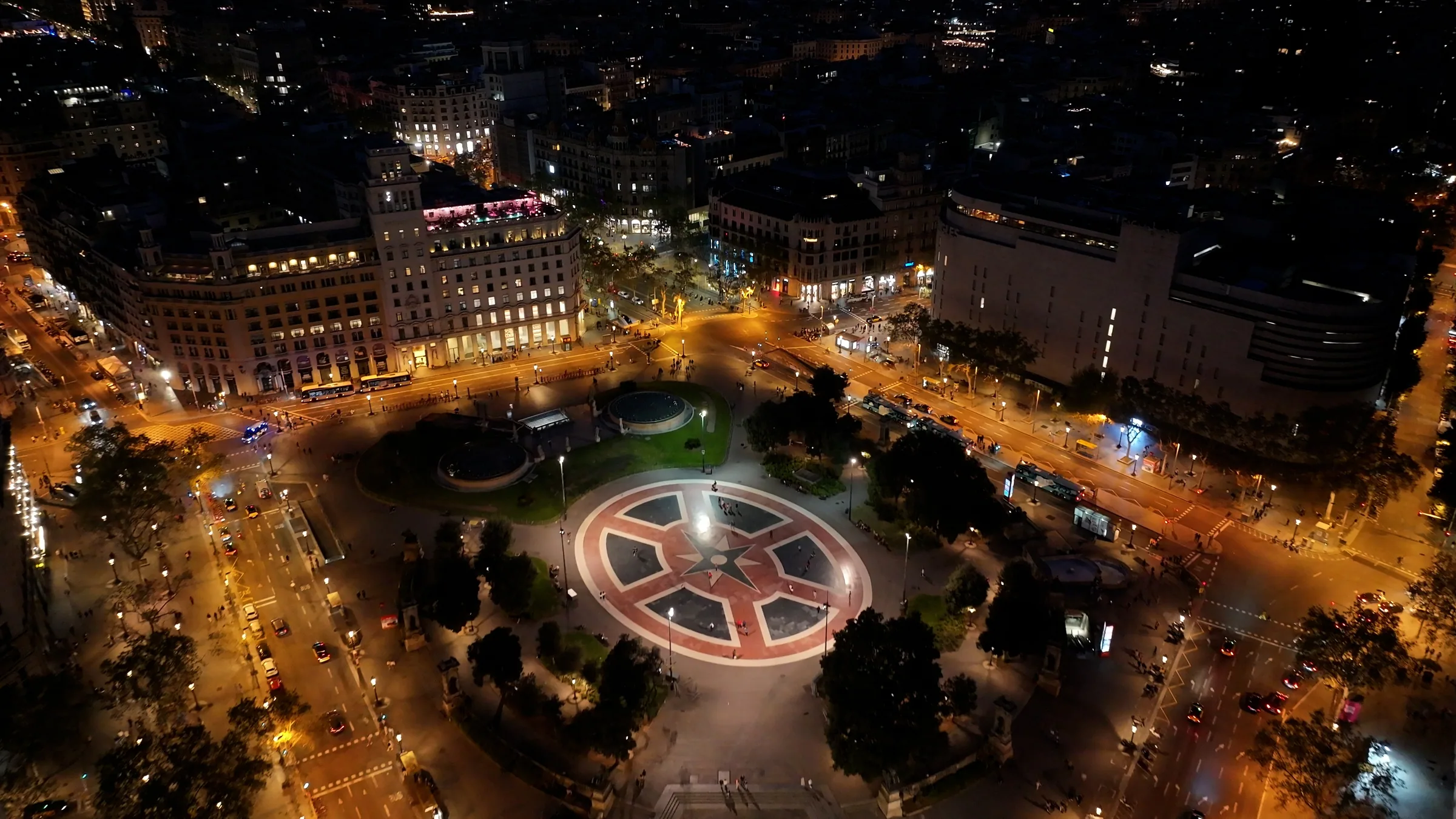 Barcelona nightlife neighborhoods — Plaça de Catalunya from the air at night, the Eixample's grid above it and La Rambla running down into the old town below