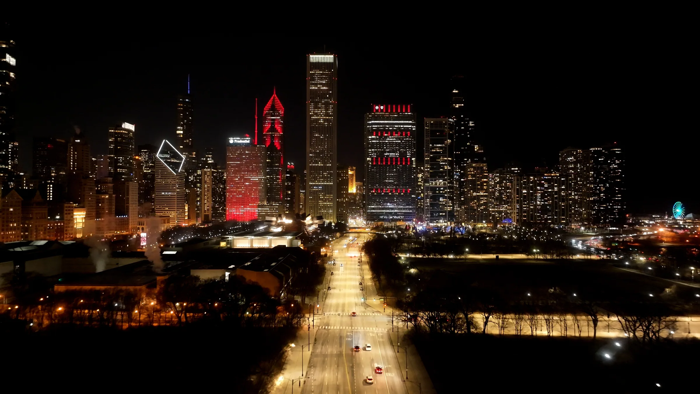 Chicago nightlife neighborhoods — Columbus Drive running north into the lit towers of the Loop at night, Grant Park dark on both sides, River North and the Gold Coast beyond