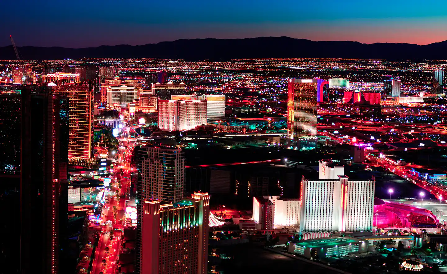 Las Vegas nightlife neighborhoods — the Strip and the valley beyond it at blue hour, seen from the north end