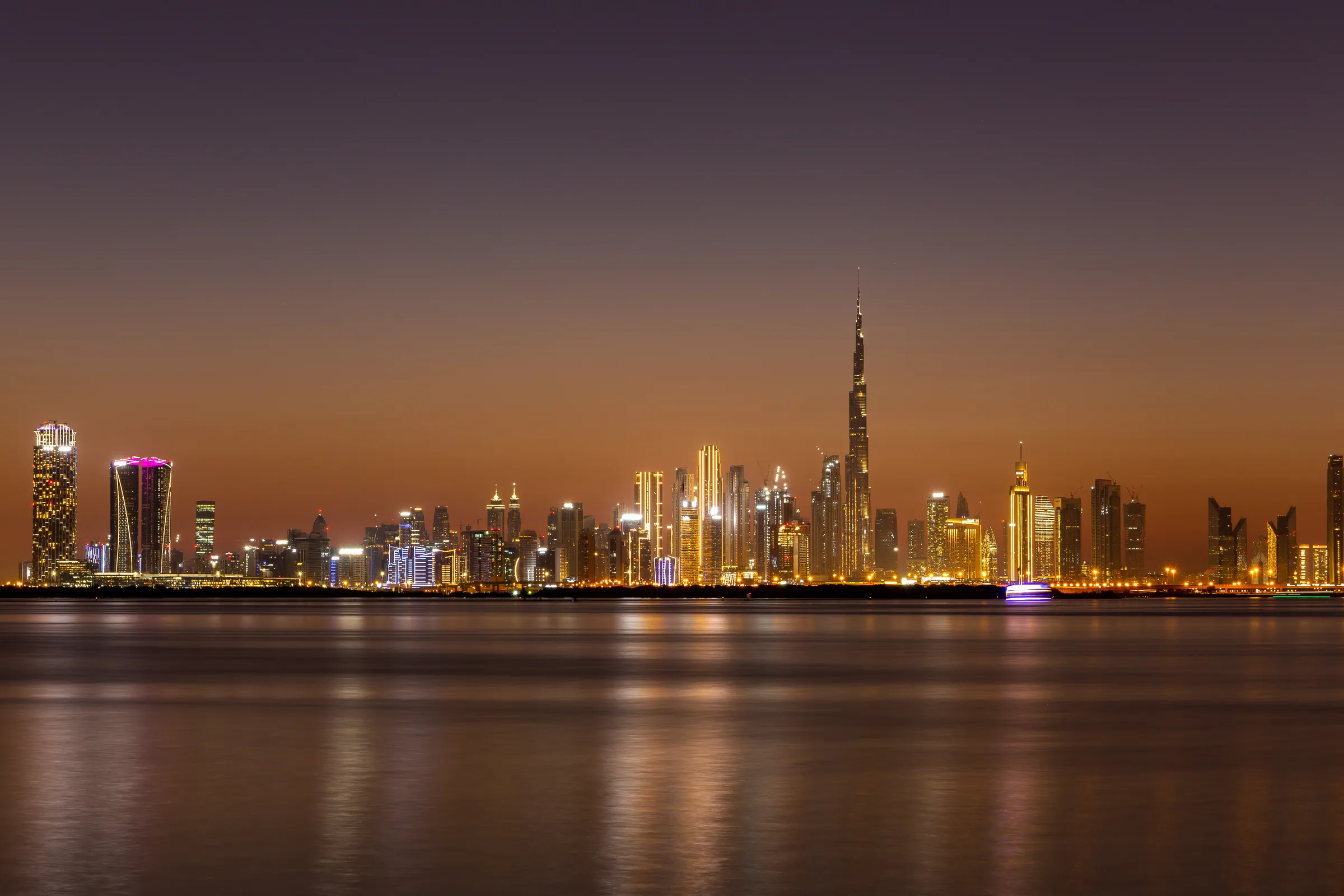 Bars in Dubai — the Business Bay and Downtown towers lit at night across the Creek, the Burj Khalifa at center, the strip of hotel lounges and DIFC cocktail bars that holds most of the city's licensed rooms