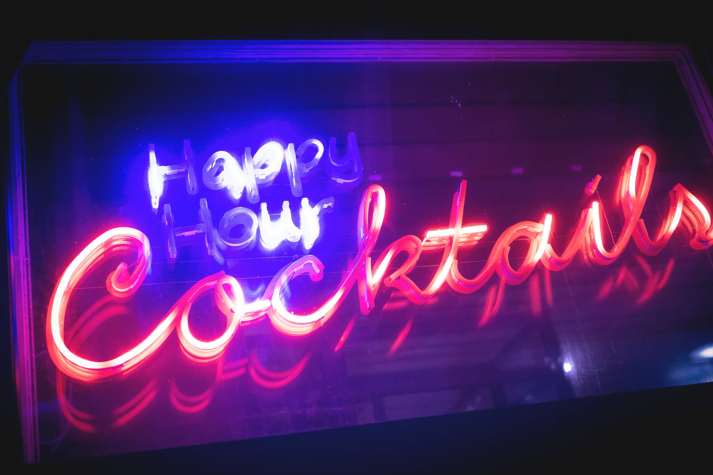 Bars in New York — a neon happy hour cocktails sign glowing in a Manhattan bar window