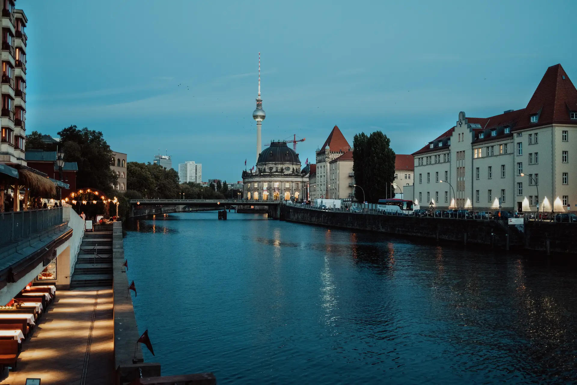 Berlin nightlife — the Spree at blue hour with the Fernsehturm over Mitte and a lit riverside bar terrace in the foreground