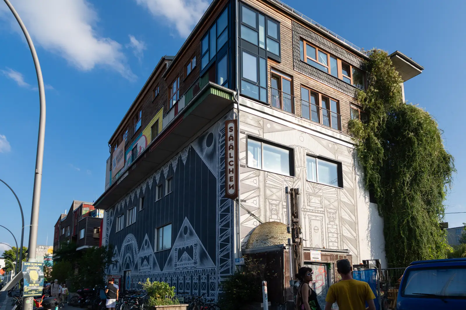 Parties in Berlin — the Säälchen party hall at Holzmarkt 25 on Holzmarktstraße, Friedrichshain, its wood-and-mural facade with people gathering out front on the Spree side